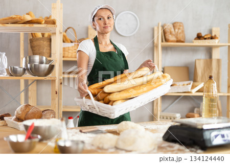 Adult woman with basket of baguettes in bakery Adult woman with basket of baguettes in bakery 134124440
