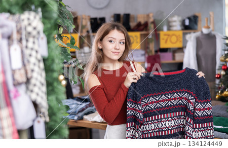 Young woman standing and choosing a sweater on the background of a Christmas tree Young woman standing and choosing a sweater on the background of a Christmas tree 134124449