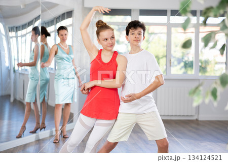 Young happy couple performing paired dance in ballroom. Dance teacher watches closely 134124521