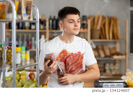 Young guy is choosing dried sausage and meat in grocery store 134124607