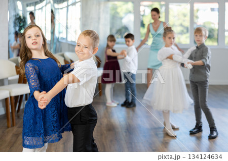 Little children in elegant dresses practicing waltz dance in school hall Little children in elegant dresses practicing waltz dance in school hall 134124634