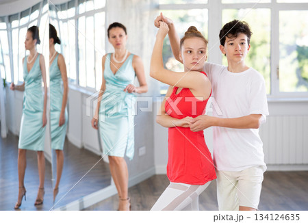 Experienced dance teacher teaching ballroom dancing to a couple of teenagers in studio 134124635
