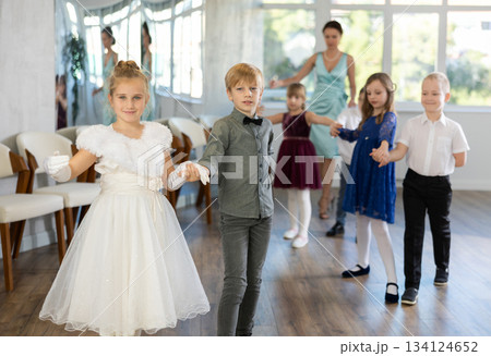 Little children in elegant dresses standing in pairs in dance pose in school hall 134124652