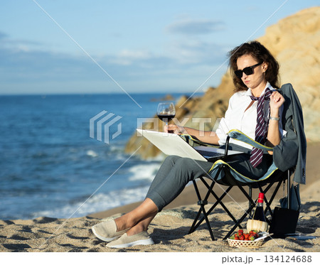 Businesswoman in sunglasses and formal attire sits on a beach chair with a laptop Businesswoman in sunglasses and formal attire sits on a beach chair with a laptop 134124688
