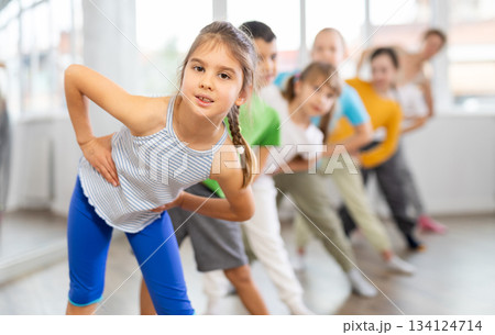 Juvenile girl engaged in choreography exercises together with children's group Juvenile girl engaged in choreography exercises together with children's group 134124714