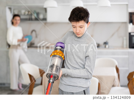 Boy vacuuming floor and his mother is washing dishes at kitchen Boy vacuuming floor and his mother is washing dishes at kitchen 134124809