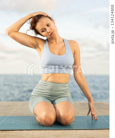 Experienced female trainer doing various exercises to warm up the body before yoga classes on seashore Experienced female trainer doing various exercises to warm up the body before yoga classes on seashore 134124908