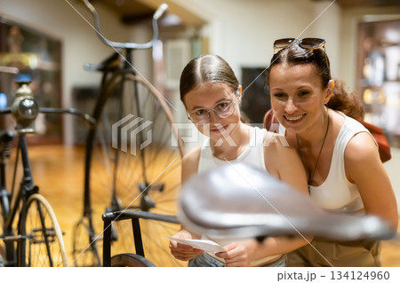 Woman and teenage girl looking at vintage bicycles in museum 134124960