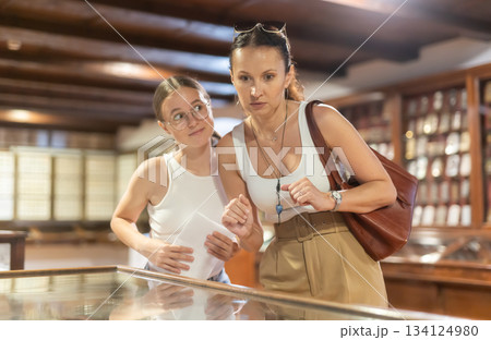 Young woman with teen daughter visitors stands near horizontal glass display case Young woman with teen daughter visitors stands near horizontal glass display case 134124980