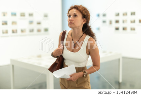 Thoughtful woman examining photographs on walls in art gallery Thoughtful woman examining photographs on walls in art gallery 134124984
