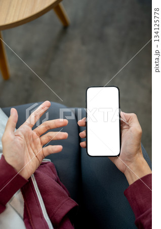 A hand holding white or blank screen smartphone aside an open palm while sitting in cafe or library. A hand holding white or blank screen smartphone aside an open palm while sitting in cafe or library. 134125778