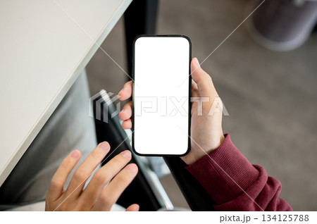 A man's hand holding white screen smartphone with fingers hovering aside at table in cafe or library A man's hand holding white screen smartphone with fingers hovering aside at table in cafe or library 134125788