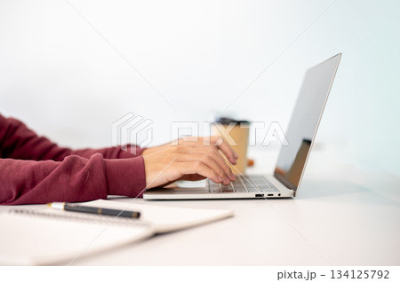 A man student's hands typing on laptop aside notebook and coffee on white table in a cafe or library A man student's hands typing on laptop aside notebook and coffee on white table in a cafe or library 134125792