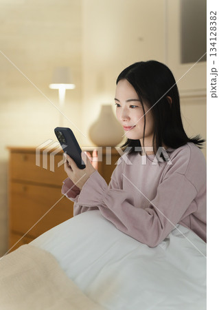 布団の中でスマートフォンを操作する若い女性　ライフスタイルイメージ 134128382