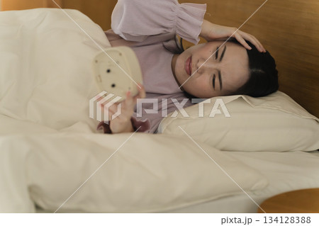 目覚まし時計を見る若い女性　ライフスタイルイメージ 134128388