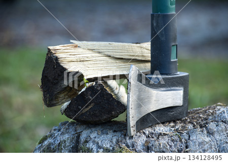 Axe and firewood on a tree stump, ready for chopping, with a blurred background. 134128495