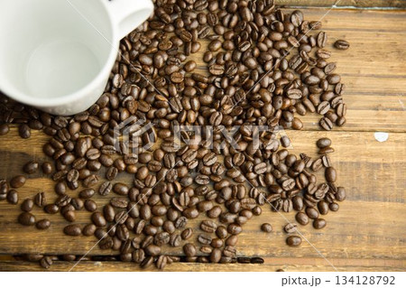Flat design showing spilled medium-roast coffee beans and white ceramic mug on rustic wooden table 134128792