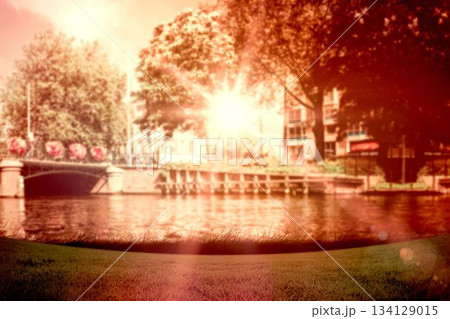 Flat design sunlit arched stone bridge is spanning canal by grassy bank, flower baskets, sun flare Flat design sunlit arched stone bridge is spanning canal by grassy bank, flower baskets, sun flare 134129015