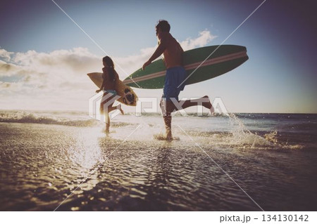 Low angle view of cheerful caucasian couple with surfboards running in sea against sky at sunset 134130142