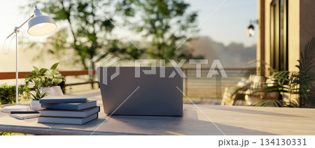 Laptop on wooden table with lamp and book aside at sunlight terrace or balcony of cafe or restaurant 134130331
