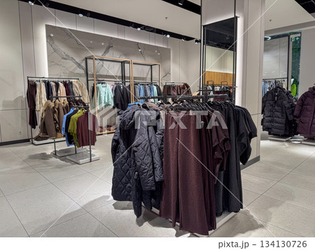 A modern clothing store interior displays racks of jackets, sweaters, and pants arranged neatly across the spacious showroom 134130726