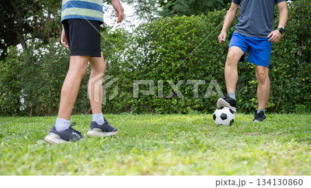 Close up of a father and son legs while playing soccer or football together in backyard or grass field. Close up of a father and son legs while playing soccer or football together in backyard or grass field. 134130860