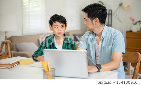 Father and son talking in front of a laptop while teaching and doing homework together. 134130910