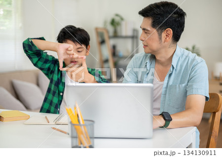 A son making finger camera while talking with his father in front of a laptop in their house. 134130911