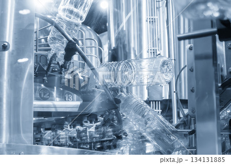 The  empty drinking water bottles  hanging on the overhead conveyor belt for filling process in the light blue scene. 134131885
