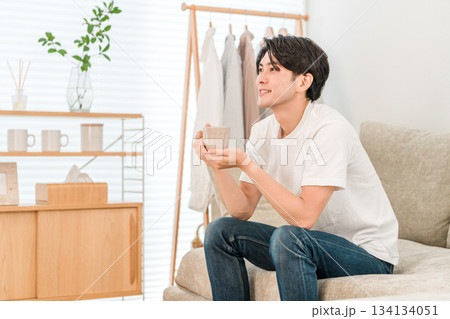 リビングのソファーに座りホットドリンク,コーヒー,紅茶を飲む若いアジア人男性 リビングのソファーに座りホットドリンク,コーヒー,紅茶を飲む若いアジア人男性 134134051