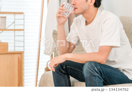 リビングのソファーに座り水ミネラルウォーターを飲む若いアジア人男性 134134702