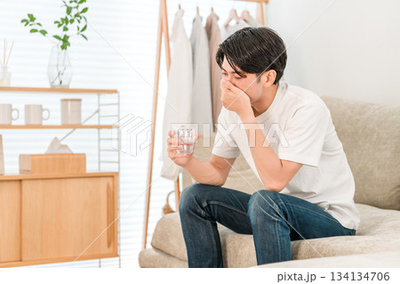 リビングのソファーに座り水ミネラルウォーターを飲む若いアジア人男性 リビングのソファーに座り水ミネラルウォーターを飲む若いアジア人男性 134134706