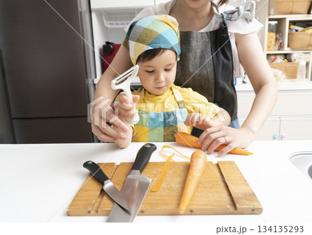 キッチンで親子で人参の皮を剥く母親と息子 134135293