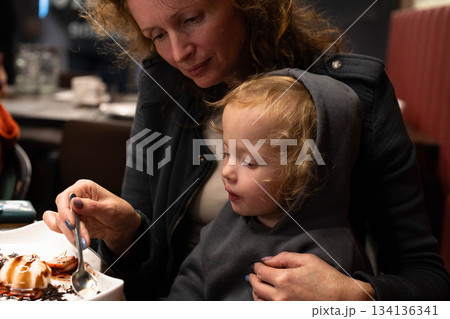 A joyful moment shared between a mother and child as they savor a delightful dessert. The warm atmosphere of the family dinner highlights their bond amidst travels, showcasing happiness and wealth. A joyful moment shared between a mother and child as they savor a delightful dessert. The warm atmosphere of the family dinner highlights their bond amidst travels, showcasing happiness and wealth. 134136341