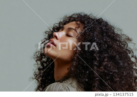 Woman with curly hair poses gracefully against a neutral background capturing natural beauty and elegance 134137515