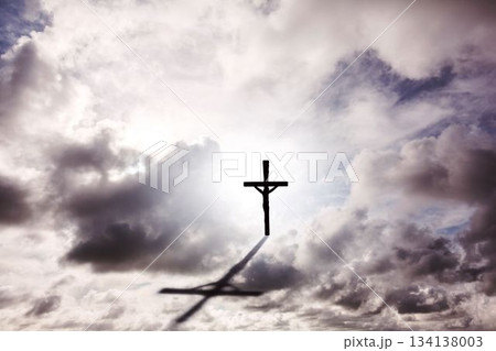 vector art showing silhouetted crucifix with Jesus standing against bright sky, casting shadow 134138003