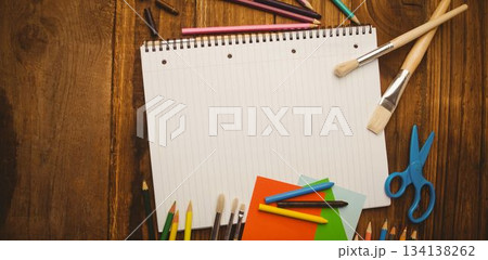 Flat design layout is showing blank notebook on wood table with pencils, paper, scissors, brushes 134138262