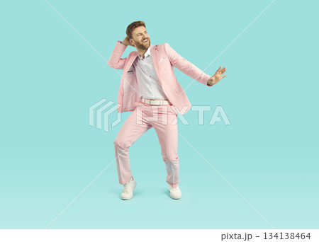Portrait of a happy, funny young man in a pink suit dancing on a blue background Portrait of a happy, funny young man in a pink suit dancing on a blue background 134138464