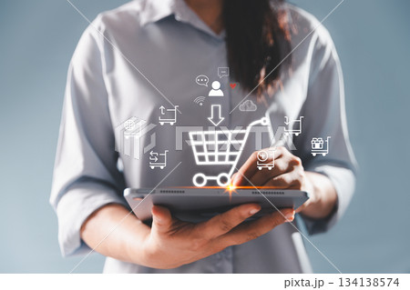 A woman using a digital tablet with glowing virtual shopping cart and ecommerce icons, representing online retail, customer interaction, mobile purchasing and modern digital commerce technology. A woman using a digital tablet with glowing virtual shopping cart and ecommerce icons, representing online retail, customer interaction, mobile purchasing and modern digital commerce technology. 134138574