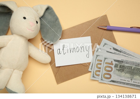 Toy bunny and envelope with word Alimony and money on beige background Toy bunny and envelope with word Alimony and money on beige background 134138671