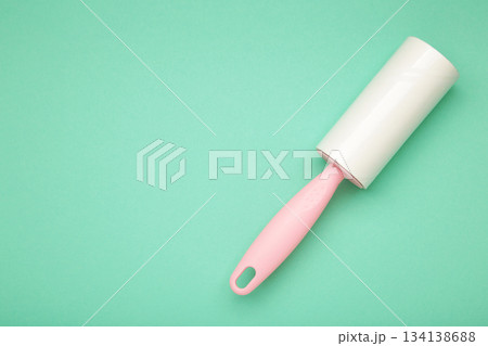 Cloth fabrics cleaner lint roller brush with paper roll on mint background. Sticky roller, pet cat dog fur dust hair remover Cloth fabrics cleaner lint roller brush with paper roll on mint background. Sticky roller, pet cat dog fur dust hair remover 134138688