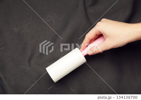 Woman cleaning black clothes background texture. Sticky roller, pet cat dog fur dust hair remover 134138700