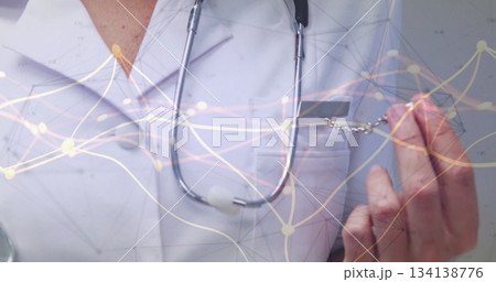 Holding badge, doctor displaying network overlay on white lab coat in clinic with stethoscope Holding badge, doctor displaying network overlay on white lab coat in clinic with stethoscope 134138776