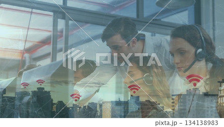 Leaning supervisor guiding headset-wearing agents at glass-paneled office desk, with Wi-Fi overlay 134138983