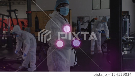 Sanitizing male worker wearing protective coverall disinfecting machines at gym, with spray wand Sanitizing male worker wearing protective coverall disinfecting machines at gym, with spray wand 134139034