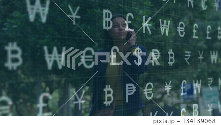 Talking businesswoman holding smartphone in landscaped courtyard, with currency symbols overlay 134139068