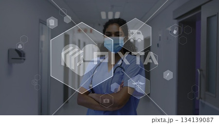 nurse crossing arms in hospital corridor, with blue scrubs mask stethoscope and hexagonal icons nurse crossing arms in hospital corridor, with blue scrubs mask stethoscope and hexagonal icons 134139087