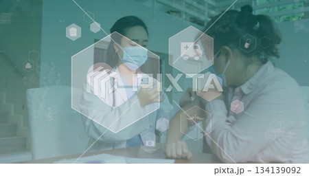 Administering doctor injecting patient arm with syringe at clinic desk, with medical icons Administering doctor injecting patient arm with syringe at clinic desk, with medical icons 134139092