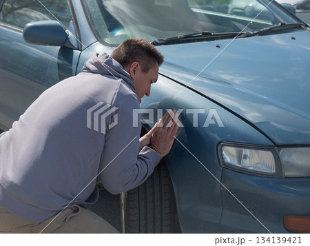 A Caucasian man tries to repair damage to a car body with his hands. 134139421