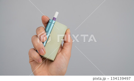Woman holding electronic cigarette on white background. Tobacco heating systems. Woman holding electronic cigarette on white background. Tobacco heating systems. 134139497